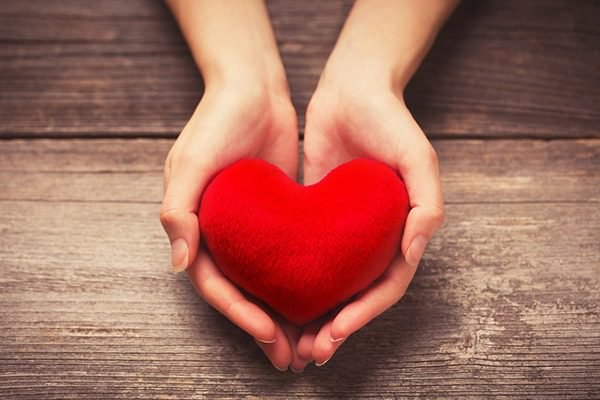 Two hands holding a red heart.