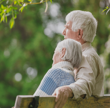 An elderly couple sitting together on a bench.